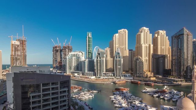 Yachts in Dubai Marina flanked by the Al Rahim Mosque and residential towers and skyscrapers aerial timelapse during all day with shadows moving fast. Modern high rise skyline with boats and wooden