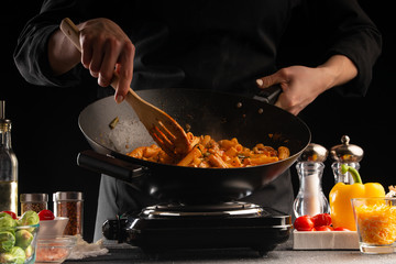 Cooking, the chef cooks pasta with sauce and vegetables in a pan, or wok, against a background of vegetables .. cooking. Recipe book, cooking and gastronomy