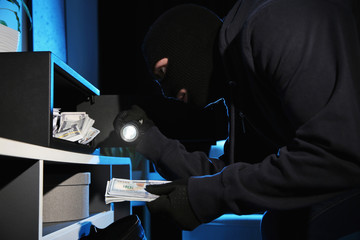 Thief taking money out of steel safe indoors at night