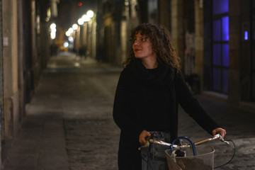 Fototapeta na wymiar Smiling young woman walking with her bike at night through the streets of Barcelona