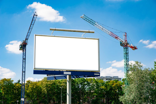 Blank white advertising billboard in front of construction cranes