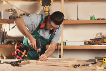 Professional carpenter twisting screw with drill at workbench