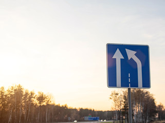 Blue road sign on sky background with sunny sunset narrowing the road to the right. Concept of warning signs about lane change, copy space