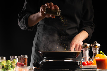 The chef fries the meat in a pan, sprinkles with seasoning. Freezes in motion. Delicious and healthy food. Vegetables and meat. Restaurant and hotel business, recipe book