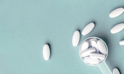 White pills in dosage spoon for drugs on a blue background, close-up