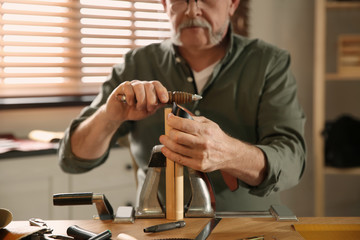 Man burnishing edges of leather belt in workshop, closeup