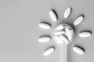 White pills in dosage spoon for drugs in the shape of a flower on a gray background, close-up