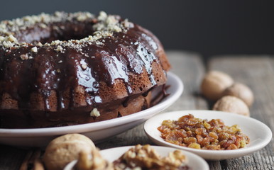 Festive homemade cakes. Round chocolate muffin, large muffin or chocolate icing cake on a wooden ancient background with nuts, raisins, and cinnamon. Place for text.