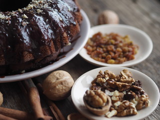 Festive homemade cakes. Round chocolate muffin, large muffin or chocolate icing cake on a wooden ancient background with nuts, raisins, and cinnamon. Place for text.