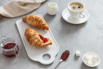 Breakfast with fresh croissants, cup of coffee and strawberry jam on a gray background, selective focus. Cafe, menu, bakery concept. Side view, copy space