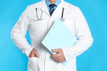 Senior doctor with clipboard on light blue background, closeup