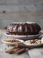 Festive homemade cakes. Round chocolate muffin, large muffin or chocolate icing cake on a wooden ancient background with nuts, raisins, and cinnamon. Place for text.