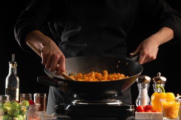 Cooking, the chef cooks pasta with sauce and vegetables in a pan, or wok, against a background of vegetables .. cooking. Recipe book, cooking and gastronomy