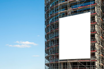 Blank white banner for advertisement hanging on the scaffolding of modern building under...