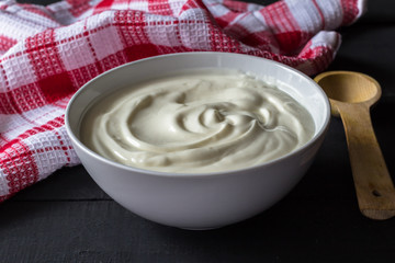 Yogurt in a white bowl on rustic black wooden table