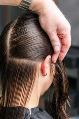 Naklejka premium Hairdresser makes hairstyle for woman, back view, close up.