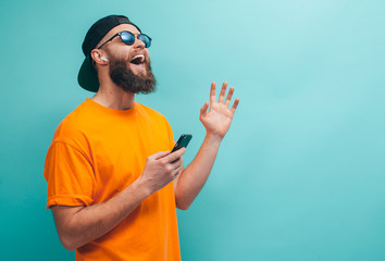Handsome hipster guy with beard wearing orange t shirt and black cap closes eyes listens loud song...