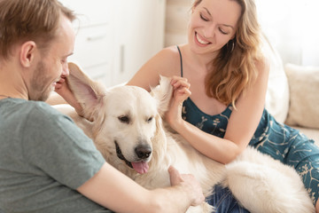 Happy family couple young girl and cute guy spends time sitting with his beloved dog in the cozy room of his country house