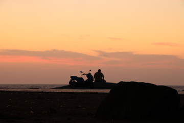 Fototapeta na wymiar The silhouette of a person sitting and watching the sunrise With motorcycle