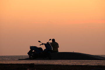The silhouette of a person sitting and watching the sunrise With motorcycle