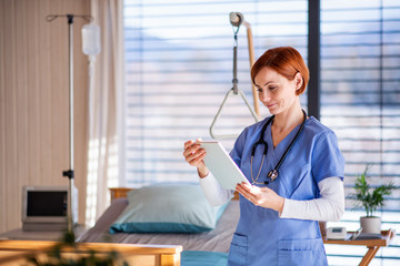 Portrait of female doctor or nurse standing in hospital room, using tablet.