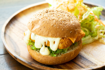 Fried fish fillet burger with vegetable salad on wood plate background