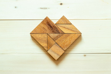 Wood tangram puzzle in heart shape on white wood background