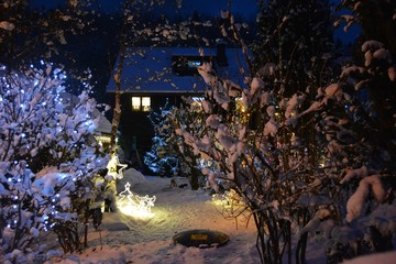 Wooden house covered with snow and christmas lights at dusk.