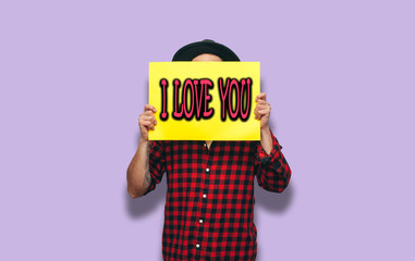 Handsome hipster man holding a blank yellow billboard or poster with blank space for your text isolated on purple background. Discount, sale, season sales.