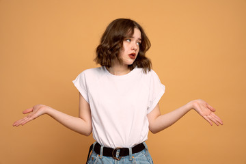 Young beautiful woman standing over orange isolated background clueless and confused expression with arms and hands raised. Doubt concept.