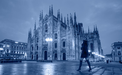 Fototapeta na wymiar Woman in black clothes with black hat is walking on the street - Duomo di Milano (Milan Cathedral) and Piazza del Duomo in the Morning, Milan, Italy