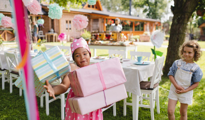 Portrait of small girl with presents outdoors in garden in summer.
