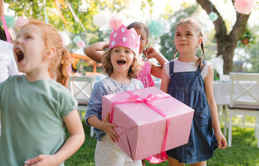 Portrait of small girl with friends and present outdoors in garden in summer.