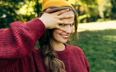 Close-up portrait of funny young blonde woman smiling broadly, wearing a sweater, and a yellow hat, posing on nature background in the park. Happy female posing outside. People travel, lifestyle.