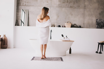 Beautiful woman relaxing in white bathrobe near bath