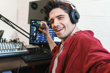 Image of young happy dj man wearing headphones working at radio station