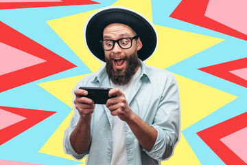 Handsome bearded guy holds smartphone and plays online games. Joyful man wearing a black stylish...