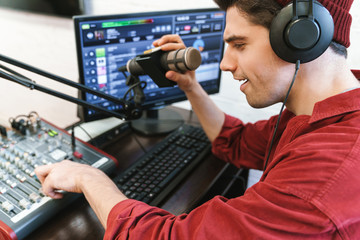 Image of young happy dj man wearing headphones working at radio station