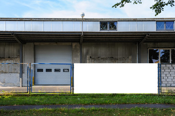 Blank white advertising banner mounted on the fence of warehouse with loading ramp
