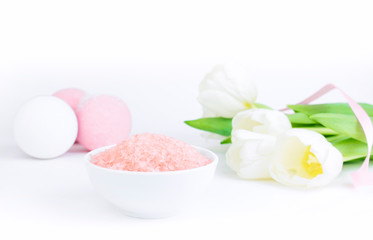 Obraz na płótnie Canvas Pink bath salt next to salt bombs and tulips, on a white gray background, are reflected on the mirror surface of the table. The concept of cosmetology, spa care, relaxation. Copy space