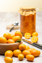 Pile of kumquat fruits, chinese tangerines, on wooden table with jam jar.