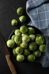 Composition with bowl of brussels sprout on black background, top view