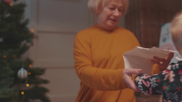 Cute family scene. Cheerful granny holding a hand of baby boy dancing together on the floor playing on holidays. At home.