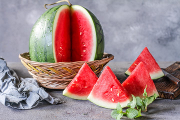 Photo of fresh watermelon with green leaves on wooden board over the table. Whole and sliced. Cutting board. Cut in halves. Dark background. Front view. Raw organic fruit. Image