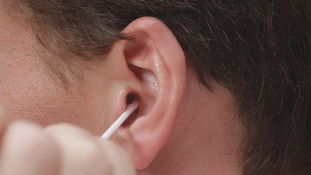 Close up portrait of man cleaning ears with cotton swab isolated over black background