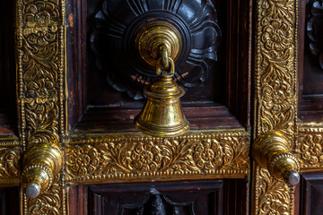 Antique bronze bell on a wooden door with inlaid Hindu temple. Close-up