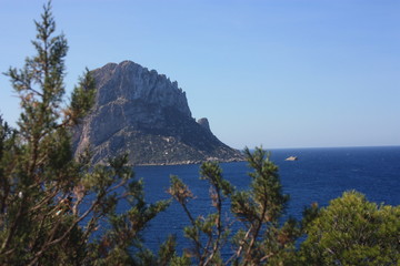 Fototapeta na wymiar The island of Es Vedra between the blue sky and the blue sea of ​​the Ibizan coasts in front of the Cala D'Hort beach in the Balearic Islands
