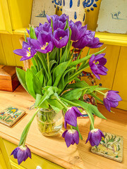 Vase of brightly coloured flowers on a yellow cottage Welsh dresser. Beautiful purple tulips close up.