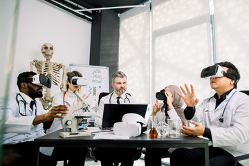 Middle aged male teacher professor has a practical class on microbiology, chemistry with group of multiethnic students, wearing vr goggles while studying cells, bacterias or chemical substances