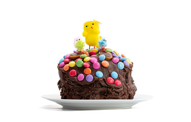 Easter cake on a white background. Fun kids chocolate cake decorated by a child with chocolate frosting covered in colorful chocolate beans and Easter chicks. Decoration sliding down sides of cake.